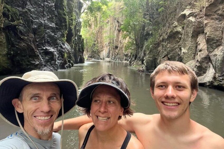 Three people in a river canyon with rocky cliffs and greenery. 1