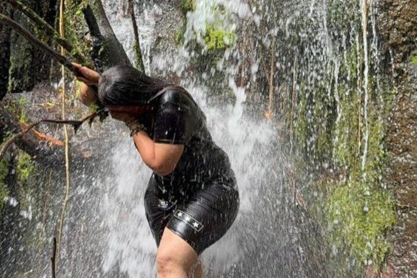 A person in a forested area, wearing a black wetsuit, holding a camera, with water splashing around. 5