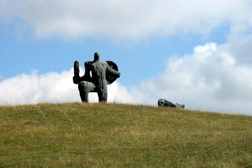 A sculpture of a figure on a grassy hill with a cloudy sky in the background. 2
