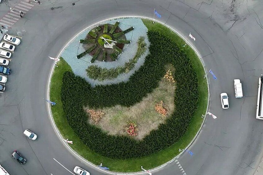 A roundabout with a central landscaped area featuring a clock and a circular pattern of trees and shrubs. 4