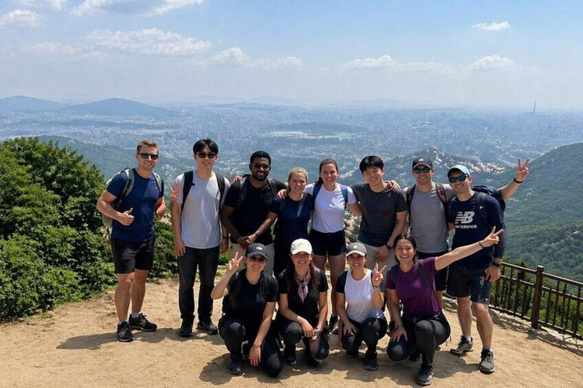 A group of people on a mountain trail with a scenic view of a city in the distance. 1