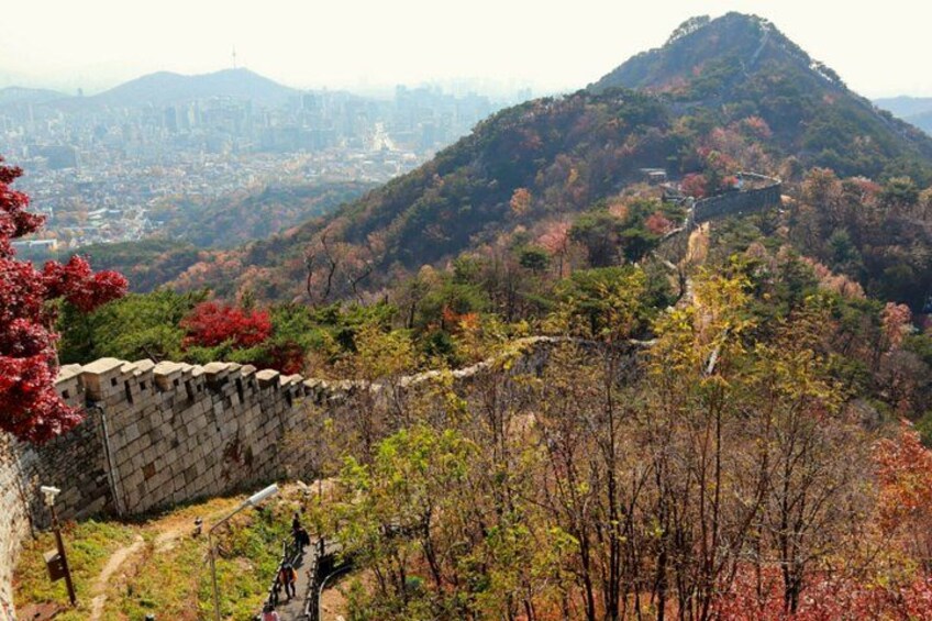 A mountainous landscape with a stone wall, autumn foliage, and a city in the background. 5