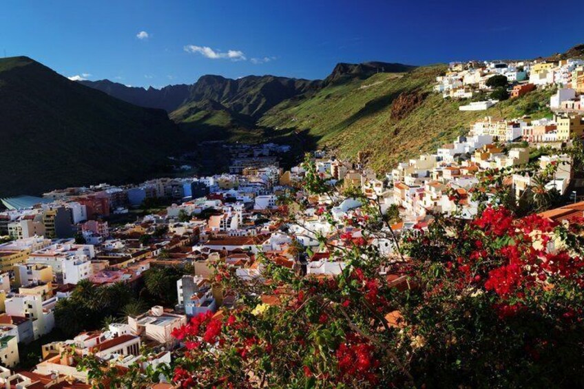 A coastal town with white buildings, red flowers, and mountains in the background. 2