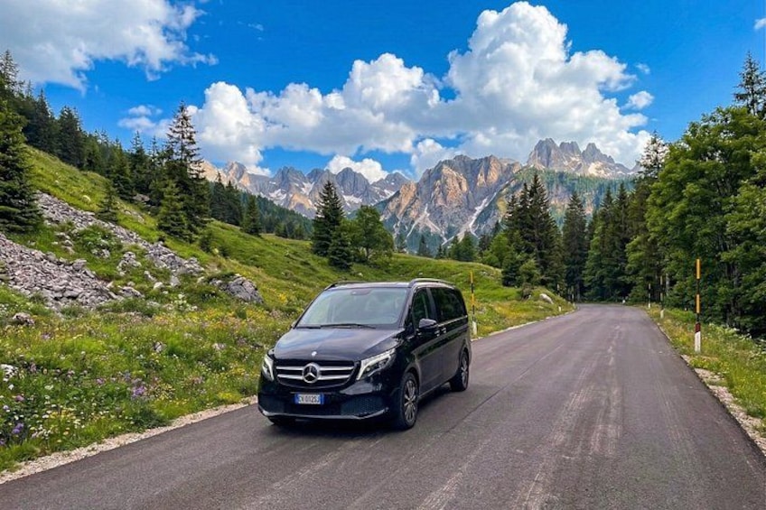 Ein schwarzes Auto auf einer Bergstraße mit blauem Himmel und Bergen im Hintergrund. 1