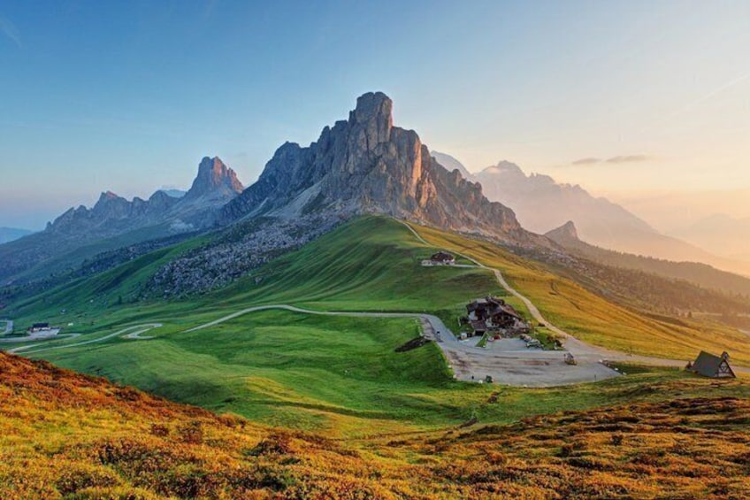 A mountain landscape with a prominent peak, a winding road, and a small building. 1