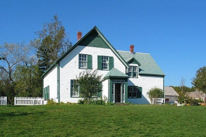 A white house with green shutters and a green roof, surrounded by a white picket fence and a grassy lawn. 1