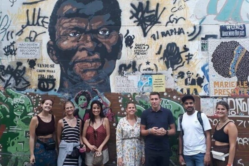 A group of people standing in front of a wall with graffiti and stickers. 5