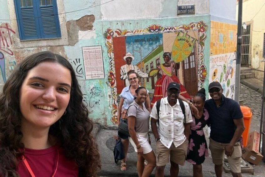 A group of people standing in front of a colorful mural with a building in the background. 2