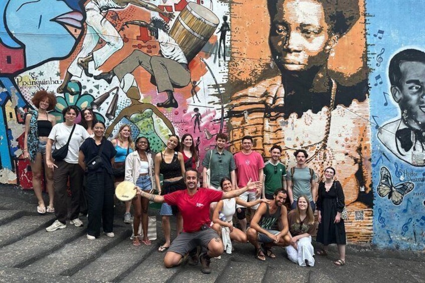 A group of people posing in front of a colorful mural with graffiti art. 3