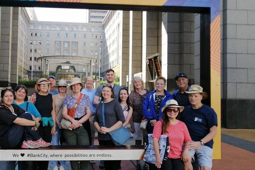 A group of people posing in front of a building with a glass facade and a cityscape in the background. 5