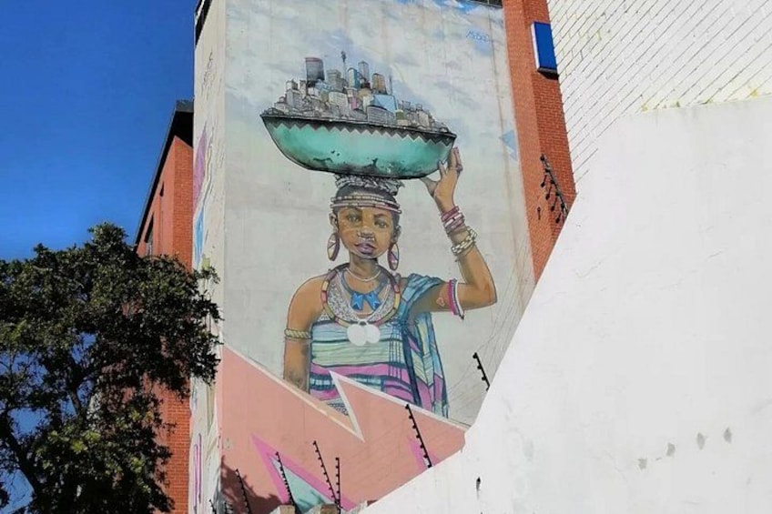 A mural of a woman carrying a large bowl on her head, with a cityscape in the background. 4