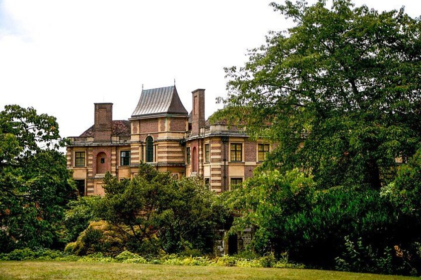A large, historic building with a brick facade, multiple chimneys, and a prominent arched window. 1