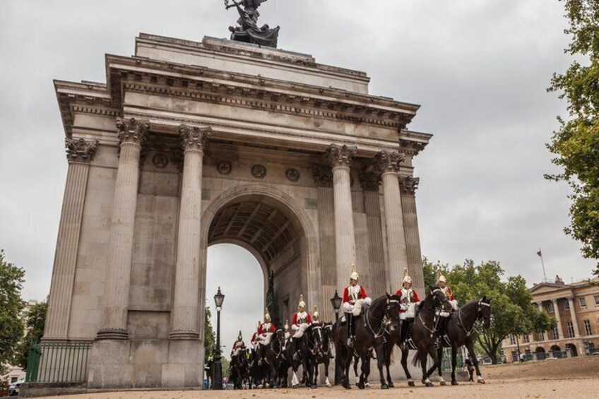 A large stone archway with statues on top and a group of mounted guards in uniform. 1