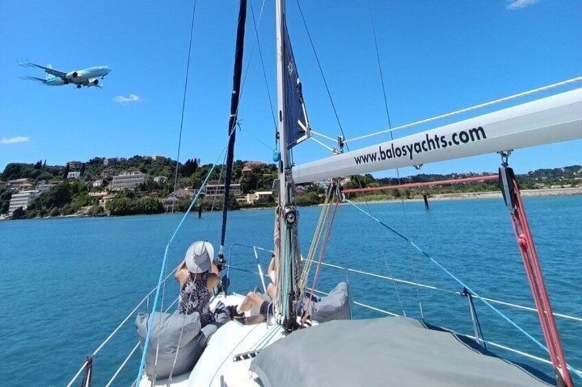 A sailboat with a website URL, calm water, a distant airplane, and a coastal town in the background. 2