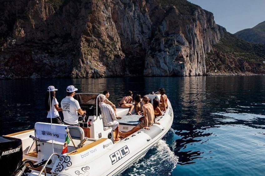 A boat with people on a calm sea, surrounded by rocky cliffs. 4