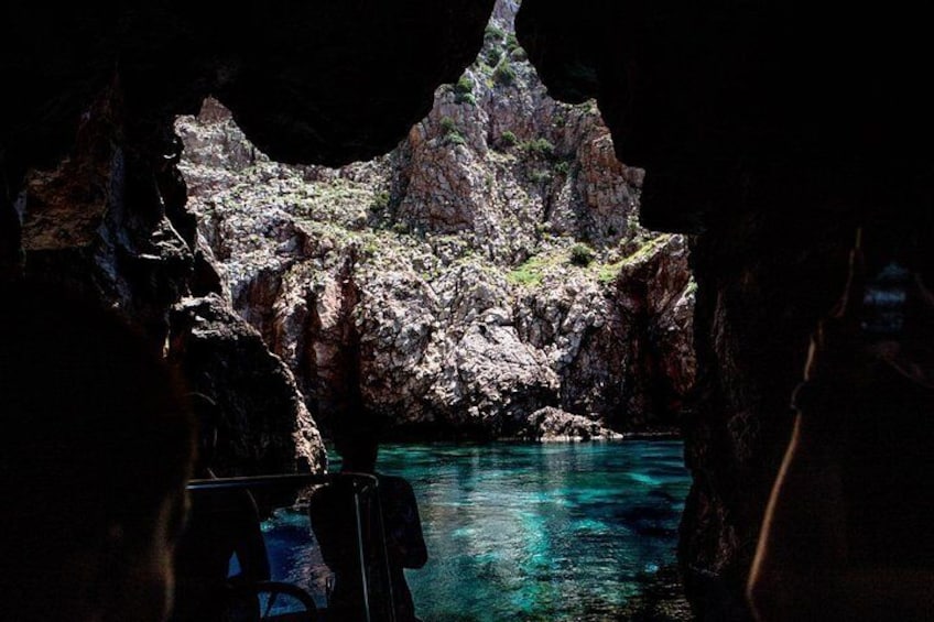 A rocky coastal landscape with clear blue water, a boat in the foreground, and a cave entrance. 3
