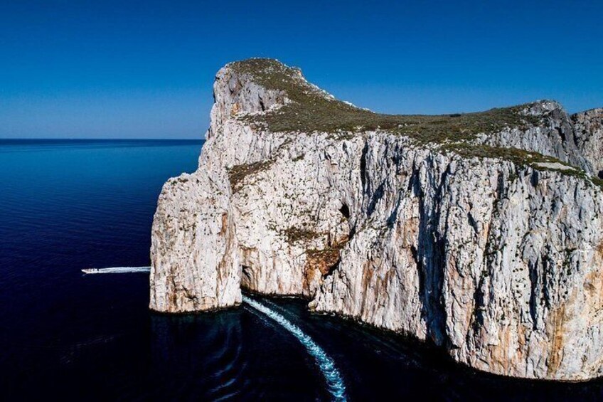 A large rock formation by the sea with a boat passing through a narrow opening. 2