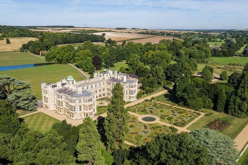 A large, historic building with a formal garden and surrounding countryside. 1