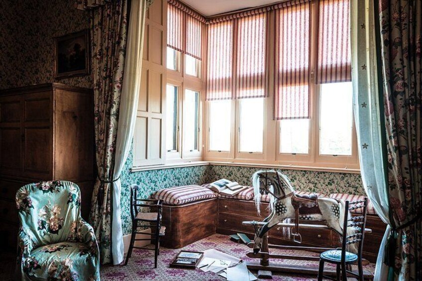 A vintage room with a wooden desk, a rocking chair, and a window with curtains. 2