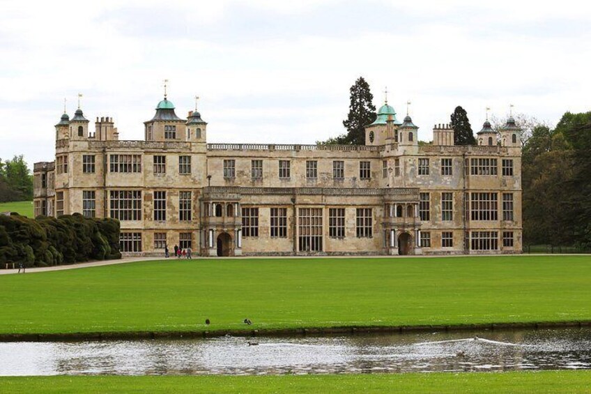 A large, historic building with multiple towers and domes, surrounded by a well-maintained lawn and a small body of water. 3