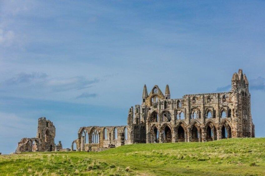 A large, historic stone cathedral with multiple arches and a grassy hill in the foreground. 5