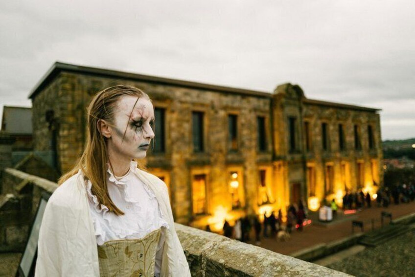 A person in historical attire standing in front of a stone building with illuminated windows. 2