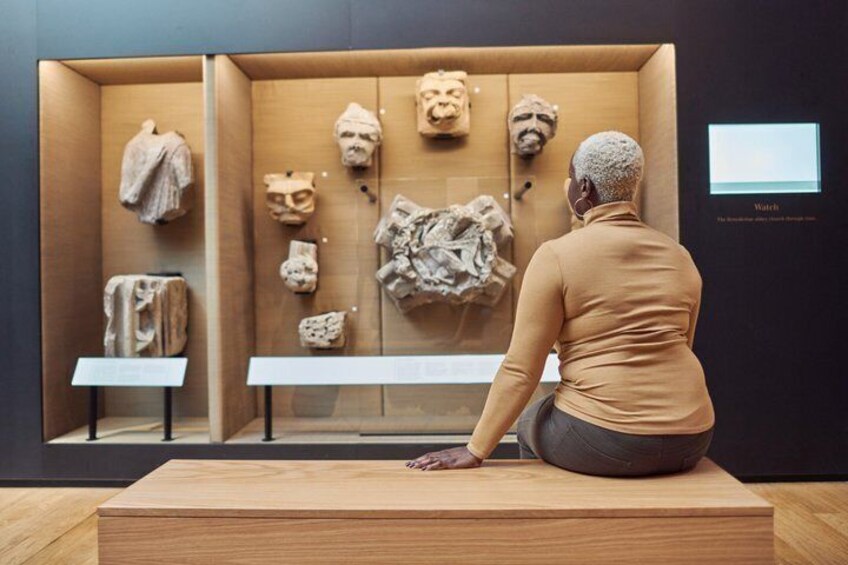 A person seated at a wooden table in a museum, observing various stone artifacts and sculptures. 4