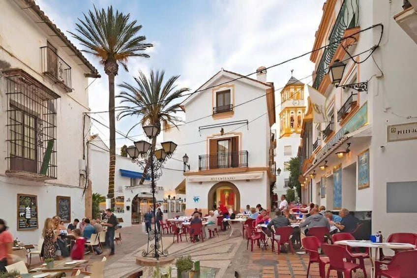 A bustling outdoor café with tables and chairs, palm trees, and traditional architecture. 1