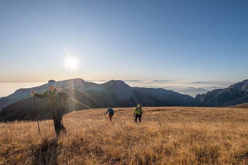 A hiker with a backpack and a child walking on a grassy field with mountains in the background. 1