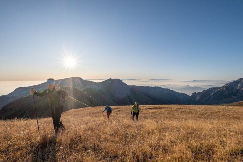 Three hikers on a grassy mountain slope with the sun shining in the background. 1