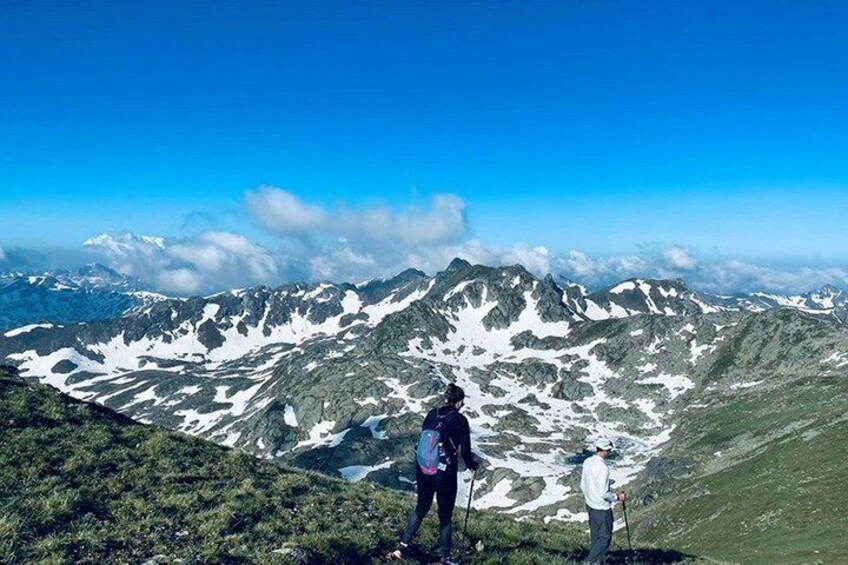 Two hikers on a mountain trail with snow patches and a clear blue sky. 3