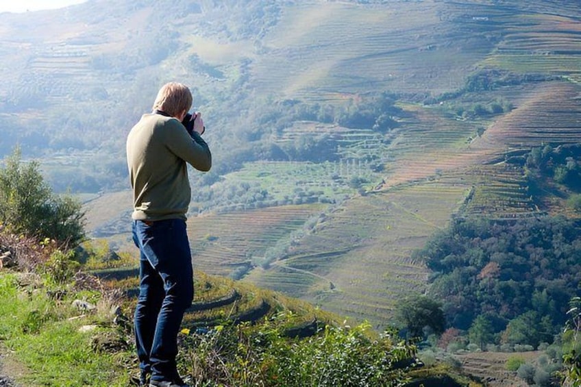 A person taking a photograph of a hilly landscape with terraced fields. 2