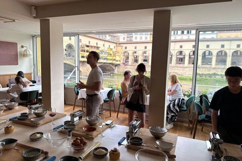 A group of people in a room with large windows overlooking a courtyard, engaged in a cooking class with cooking utensils and ingredients on the table. 2