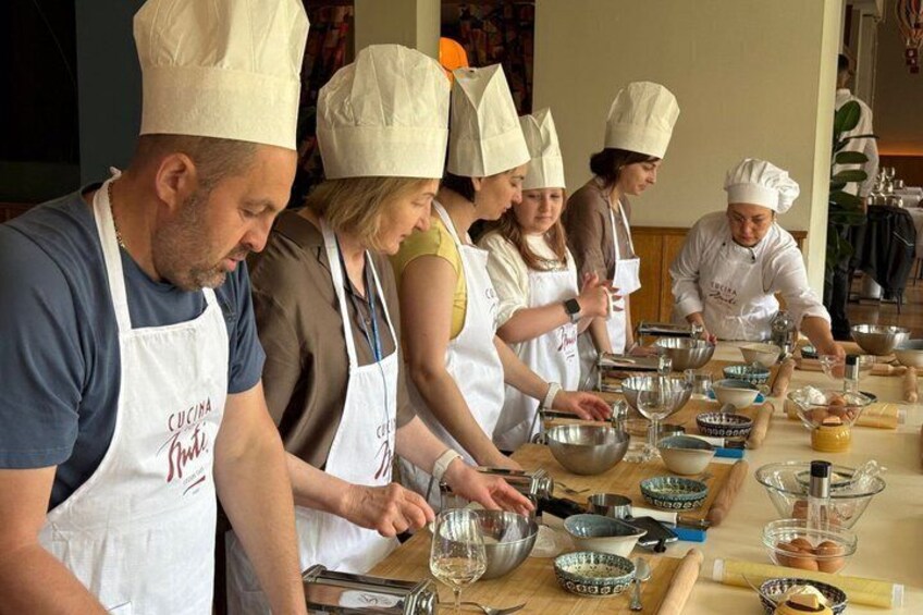A group of people in chef hats and aprons, engaged in cooking activities with various kitchen utensils and ingredients on a table. 4