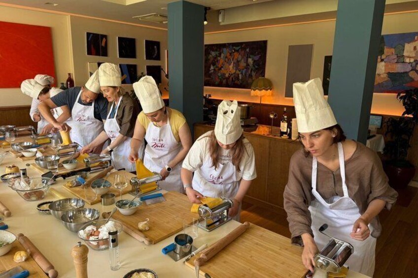 A group of people in a kitchen setting, wearing chef hats and aprons, engaged in cooking activities with various kitchen utensils and ingredients on the table. 5