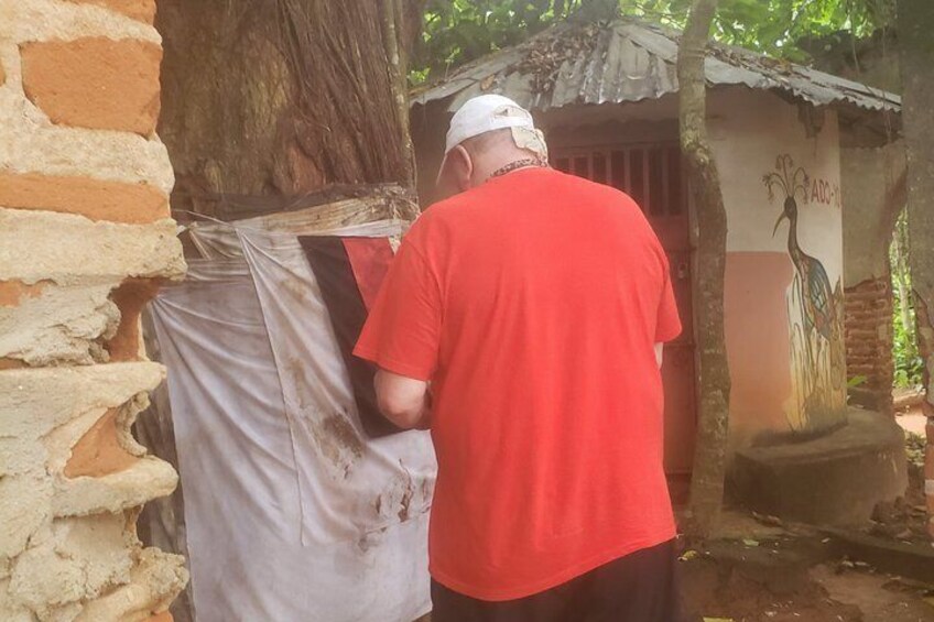 A person in a red shirt and white cap working near a tree and a building with a mural. 3