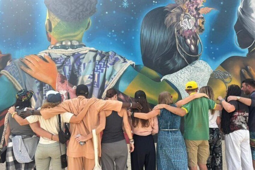 A mural with figures and people standing in front of it. 1