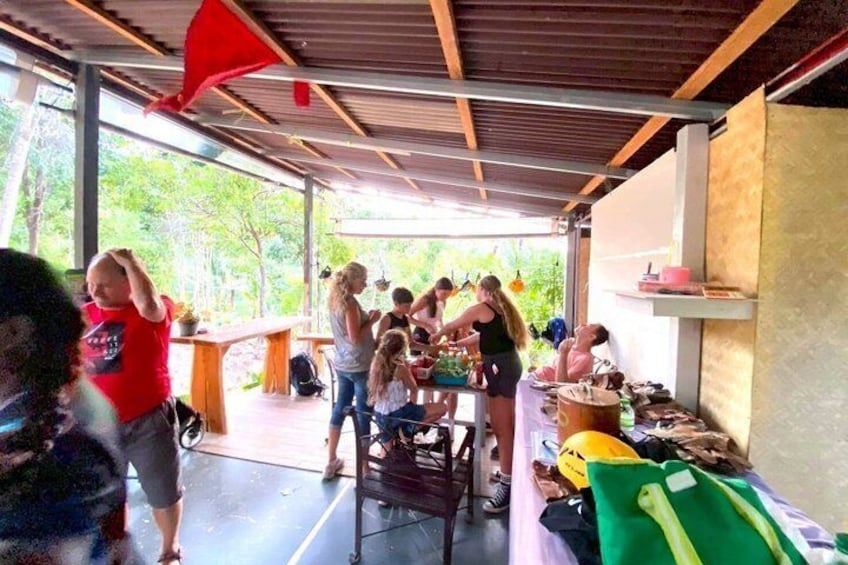 A group of people gathered under a covered area with tables and chairs, surrounded by greenery. 3