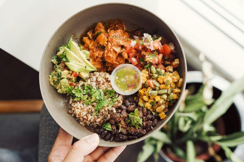 A bowl of food with various components including rice, beans, corn, and a small bowl of sauce. 1