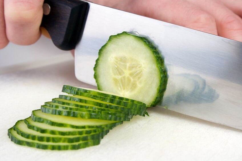 A person slicing a cucumber on a white cutting board. 3