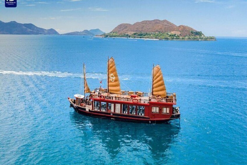 A red boat with sails on a calm sea with mountains in the background. 3