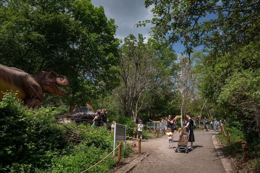 A dinosaur exhibit surrounded by lush greenery and a pathway with visitors. 3