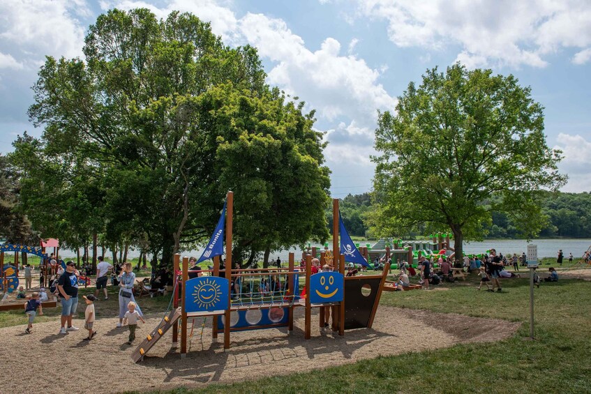 A playground with slides and climbing structures, surrounded by trees and a lake. 2