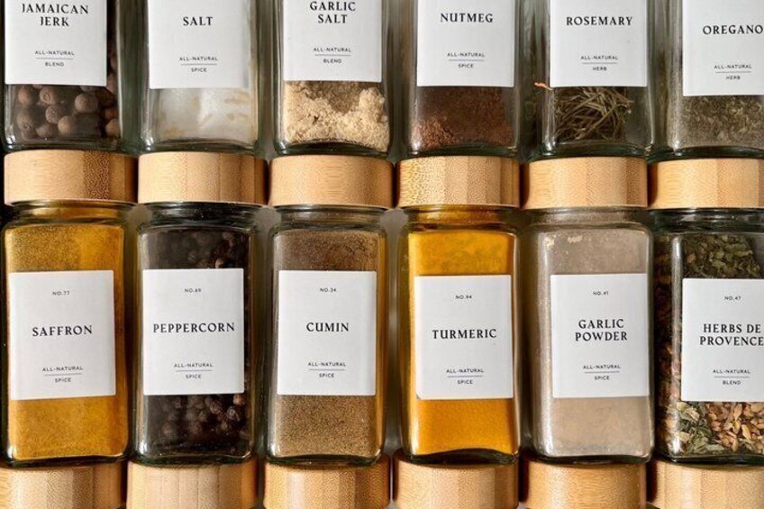 A collection of glass spice jars with labels, including Jamaican jerk, saffron, and peppercorn. 2