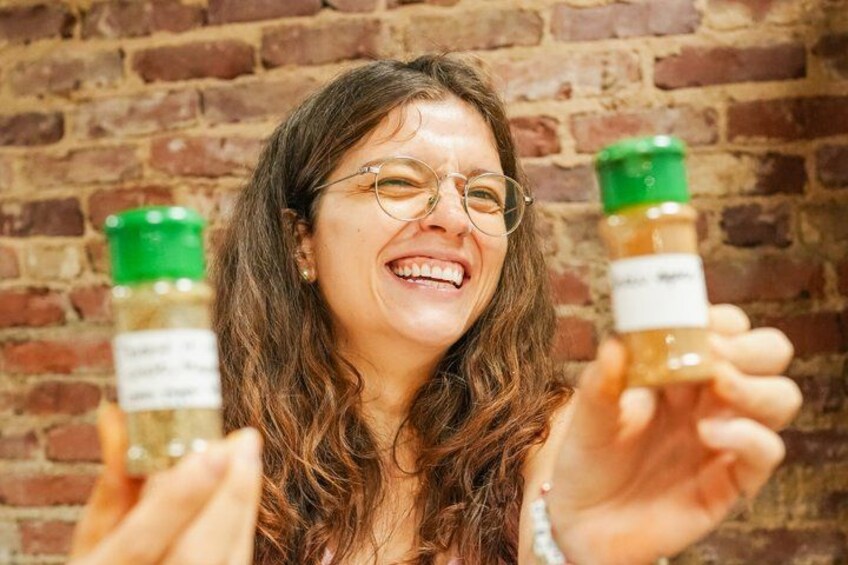 A person holding two jars with labels, against a brick wall background. 1