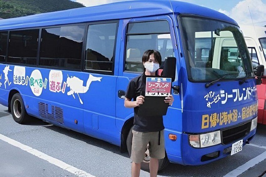 A blue bus with Japanese text and graphics, parked on a road with a mountainous background. 2