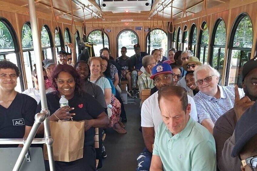 A bus interior with passengers seated and standing, large windows, and a metal pole. 5