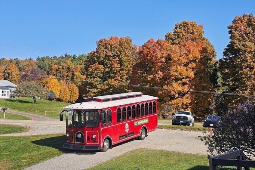 A red vintage bus parked on a driveway with autumn trees in the background. 1