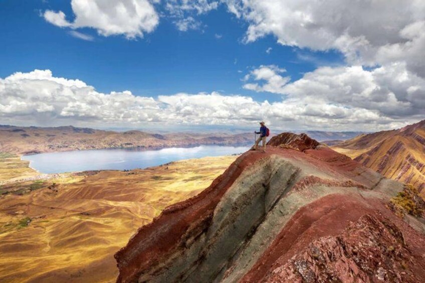 Un excursionista en una cresta montañosa roja y amarilla, con un lago al fondo. 3