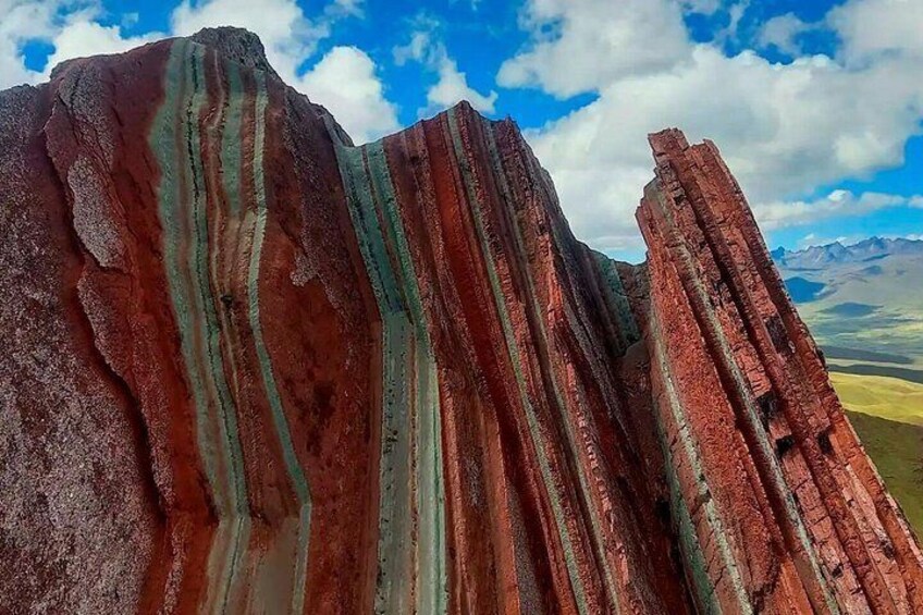A mountain with red and green striations, a clear sky, and distant mountains. 4